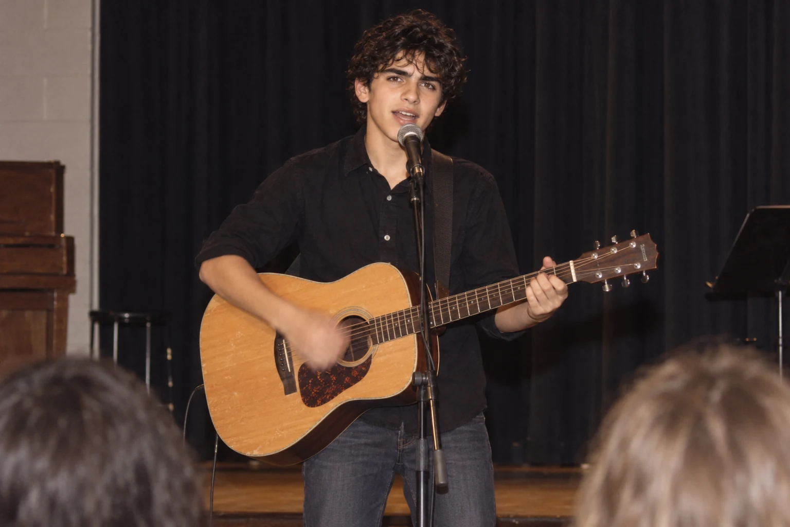 An imagined school arts-night photograph of teenage Teddy singing and playing an acoustic guitar onstage